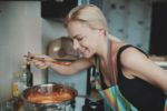 Blonde women in kitchen with apron on tasting soup